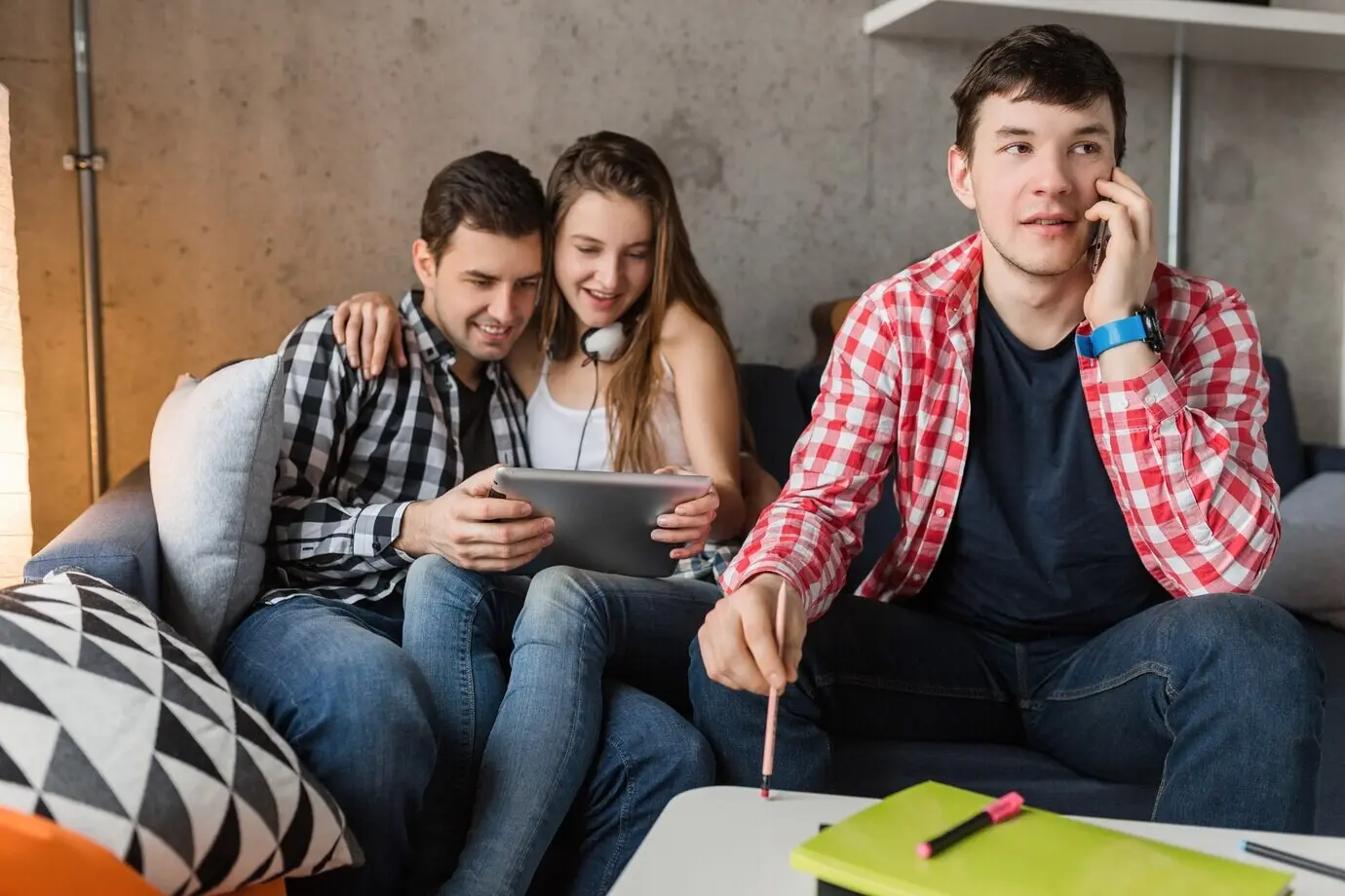 Fröhliche junge Leute nutzen ein Tablet, Studierende beim Lernen, haben Spaß, Freunde feiern zu Hause, Hipster-Gruppe zusammen, zwei Männer, eine Frau, lächelnd, positiv, Online-Lernen, ein Mann telefoniert